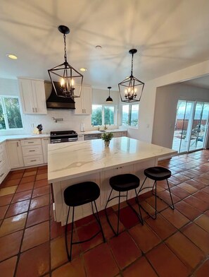 A spacious kitchen with a large island, white cabinets, and black bar stools.