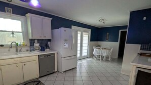 Una cocina amplia con armarios blancos, refrigerador, pileta y comedor con mesa y sillas.