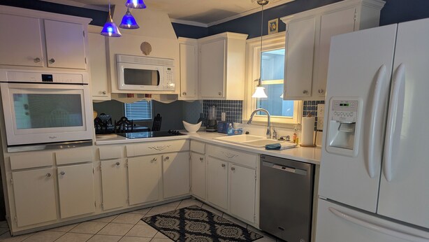 Una cocina con armarios blancos, microondas, refrigerador y lavavajillas.
