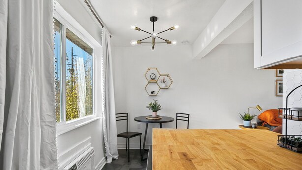 A modern kitchen with a wooden table, white walls, and a ceiling light fixture.