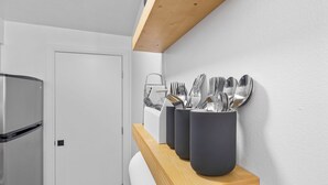 A modern kitchen with a wooden shelf holding utensils and a refrigerator.