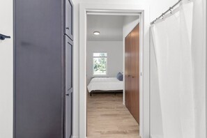 A narrow hallway leading to a bedroom with a bed, a window, and a door.