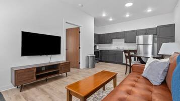 A modern living room with a flat-screen TV, wooden entertainment unit, brown leather sofa, and a wooden coffee table.