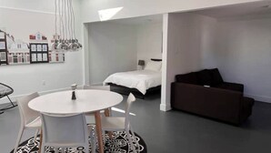 Ein modernes Zimmer mit einem runden Tisch, einem Bett, einer Couch und einer Wandleuchte.