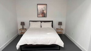 Une chambre avec un grand lit, deux tables de chevet et un tableau encadré au mur.