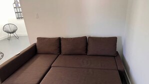 Un canapé marron avec une partie allongée, dans une pièce dont le mur est blanc et où se trouve un petit fauteuil.