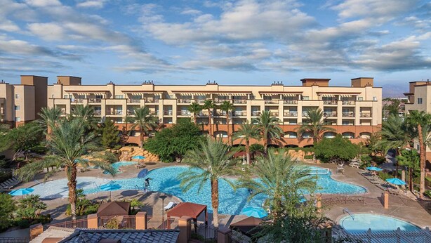Un hotel con varias piscinas, palmeras y un cielo despejado.