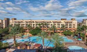 Ein Hotel mit mehreren Swimmingpools, Palmen und blauem Himmel.