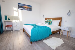 Een slaapkamer met een bed, nachtkastje, kapstok, spiegel en een schilderij aan de muur.