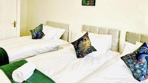 Habitación de hotel con tres camas individuales, cada una con ropa de cama blanca y almohadones decorativos.