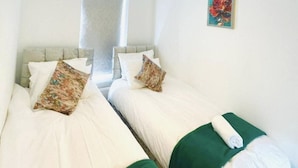 Una habitación con dos camas, cada una con ropa de cama blanca y almohadones verdes.