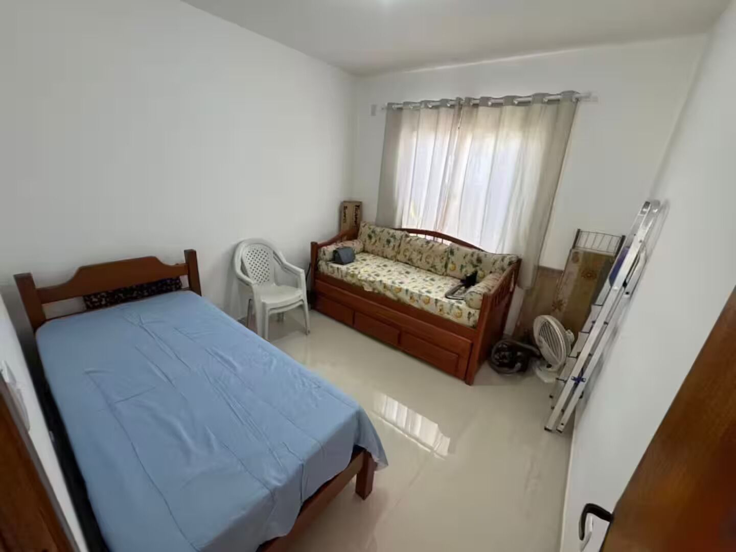 A bedroom with a bed, a sofa, a chair, a mirror, and a radiator.