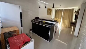 Una cocina moderna con una isla central, iluminación colgante y vistas a una sala de estar con sofá y cortinas.