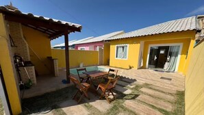 Un patio con mesa y sillas, una piscina pequeña y un edificio amarillo con techo de tejas.