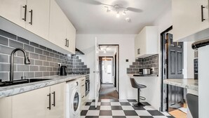 Een kleine keuken met een zwart-wit geruite vloer, een wasmachine en een barkruk.