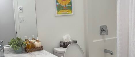 A bathroom with a toilet, sink, shower, and a framed sunflower artwork.