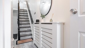 Un couloir avec un escalier, un radiateur blanc, un miroir et une porte.