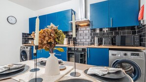 Une cuisine moderne avec des meubles bleus, un four encastré, un four à micro-ondes et un lave-linge Samsung.