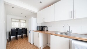 A modern kitchen with white cabinets, a wooden countertop, and a sink. There is a dining area with a table and chairs in the background.