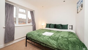 A bedroom with a bed, a window with curtains, a radiator, and a wall-mounted picture.