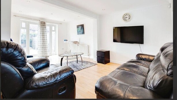 A modern living room with leather sofas, a glass coffee table, and a flat-screen TV mounted on the wall.