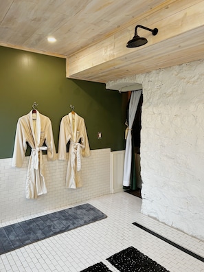Un baño con dos albornoces blancos colgados en ganchos, un cabezal de ducha y suelo de baldosas.