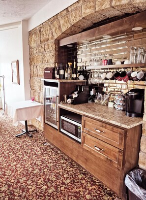 A bar area with a stone wall, wine bottles, glasses, and a microwave.