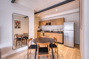 A compact kitchen with wooden cabinets, a stainless steel refrigerator, and a dining area with a round table and chairs.