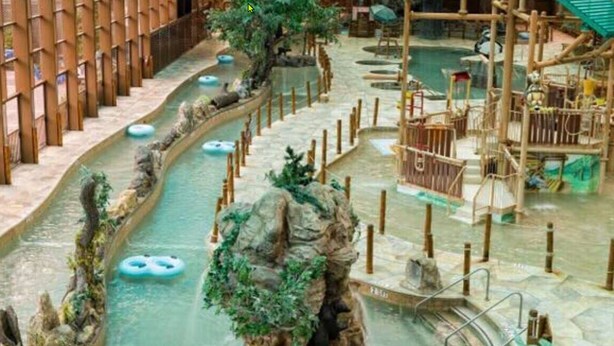 Ein großer Wasserpark mit mehreren Pools, Holzspielgeräten und einer zentralen Felsformation.