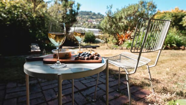Un tavolo con due bicchieri di vino bianco, un piatto di cibo e una sedia di metallo in un giardino.