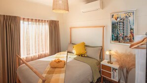 Una camera d'albergo con un letto, un comodino, una lampada, una finestra con tende e un condizionatore d'aria a muro.