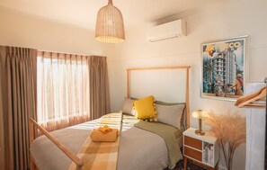 Hotelkamer met een bed, nachtkastje, lamp, raam met gordijnen en een wandairconditioner.