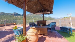 Eine Terrasse mit Tisch, Stühlen, einem Reetdach und Blick auf Berge.