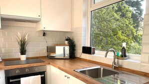 A kitchen with white cabinets, a wooden countertop, a built-in oven, a microwave, a sink, and a window with a view of trees.