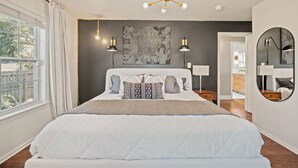 A bedroom with a large bed, two bedside tables, a ceiling light fixture, a wall-mounted mirror, and a window with curtains. - Bright & Stylish Home near Uptown - 3BR 2B + Outdoor (Charlotte)