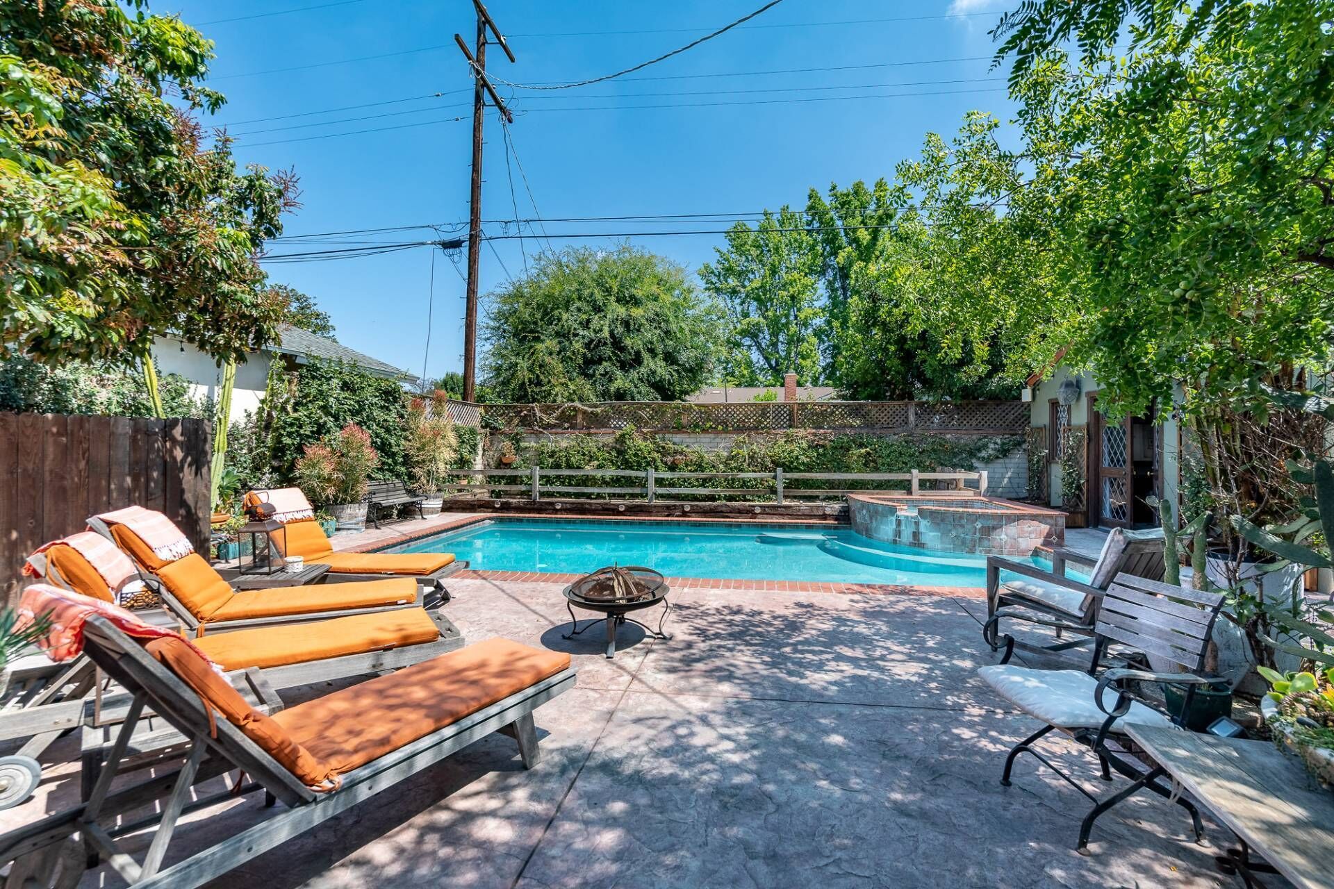Soak up the sun by the sparkling swimming pool in this gated lush backyard, complete with lounge chairs and a central fire pit.