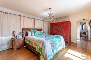 Um quarto com cama de madeira, um candelabro, um guarda-roupa vermelho e uma mesa de cabeceira de madeira.