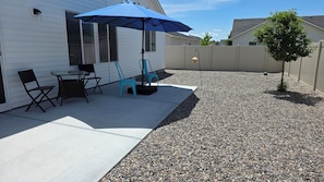 Une terrasse avec une table et des chaises, un parasol bleu et un petit arbre.