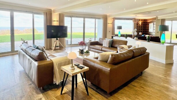 A spacious living room with a large TV, leather sofas, and a view of the outdoors. - Whitewater, with expansive sea views and hot tub (Westward Ho!)