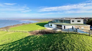 A modern house with a curved roof, large windows, and a view of the sea. - Whitewater, with expansive sea views and hot tub (Westward Ho!)