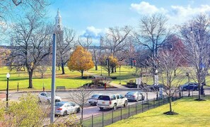 A park with a clock tower, a paved walkway, and parked cars.