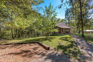 A cabin surrounded by dense forest with a gravel path leading to the entrance.