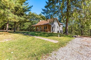 A cabin with a sloped roof, surrounded by trees, and a gravel driveway.