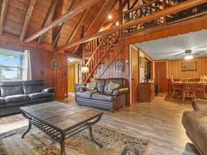 A wooden interior with a staircase, leather sofas, a dining table, and a coffee table.