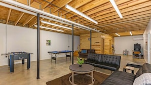 A spacious indoor area with a high ceiling, exposed wooden beams, a foosball table, a pool table, and a comfortable seating area with a sofa and a coffee table.
