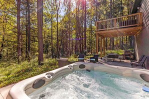 Ein Whirlpool, umgeben von einem Wald, mit einer Holzterrasse und Gartenmöbeln.