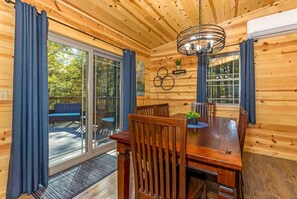 Eine Holzhütte mit Essbereich, ausgestattet mit einem Holztisch und Stühlen, einer Deckenleuchte und einer Glastür zum Außenbereich.