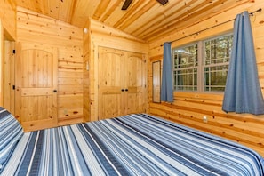 Ein Zimmer einer Holzhütte mit einem Bett, zwei Türen und einem Fenster mit Vorhängen.