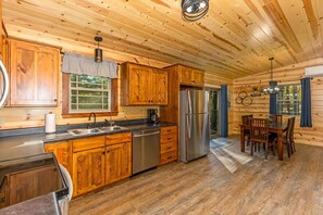 A wooden cabin interior with a kitchen, dining area, and a large window.