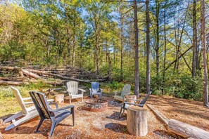 Een bebost kampeerterrein met Adirondack-stoelen rond een centraal aangelegde vuurkuil.
